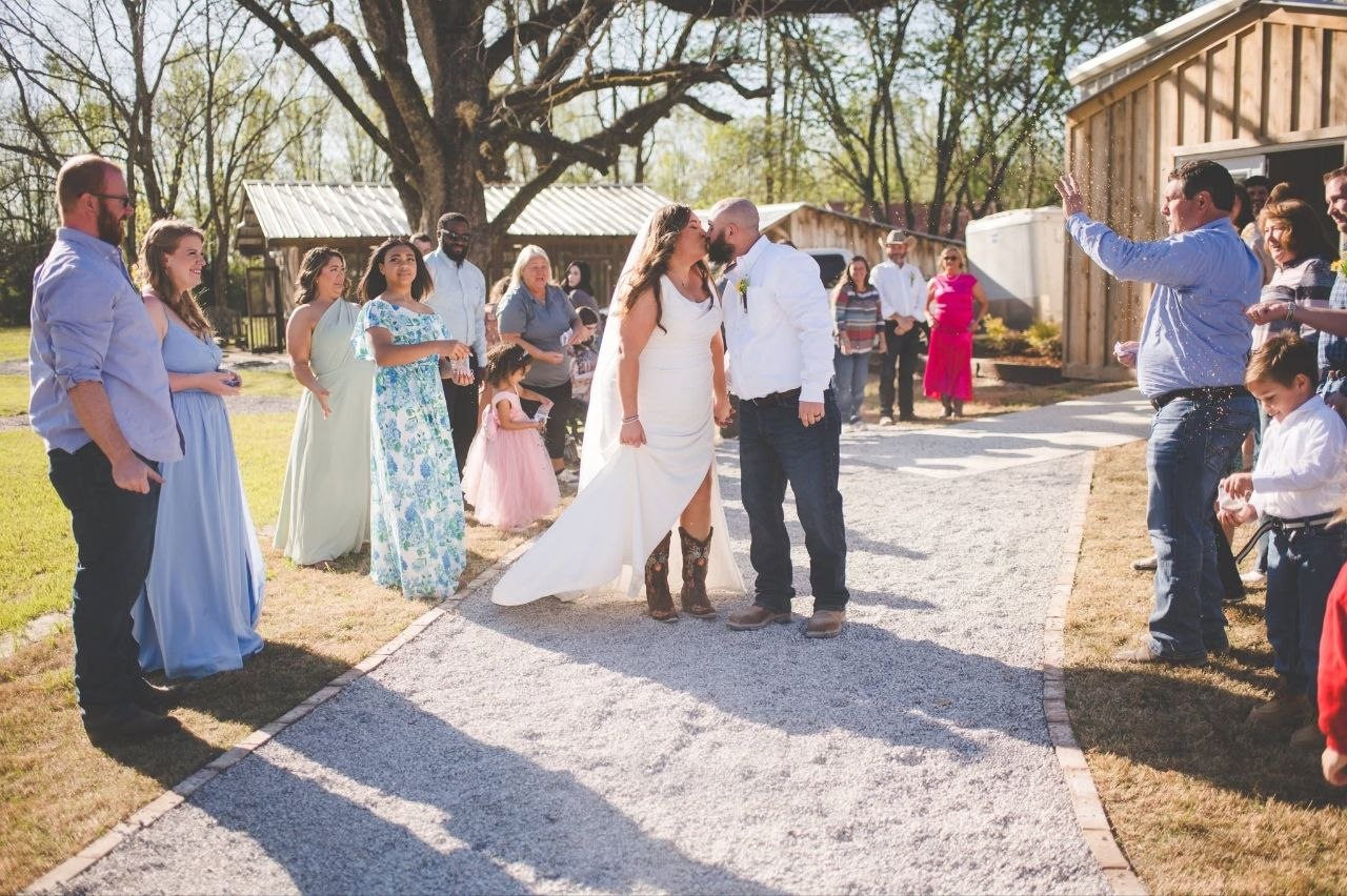 Bride and groom share a kiss while family watches on the ceremony path