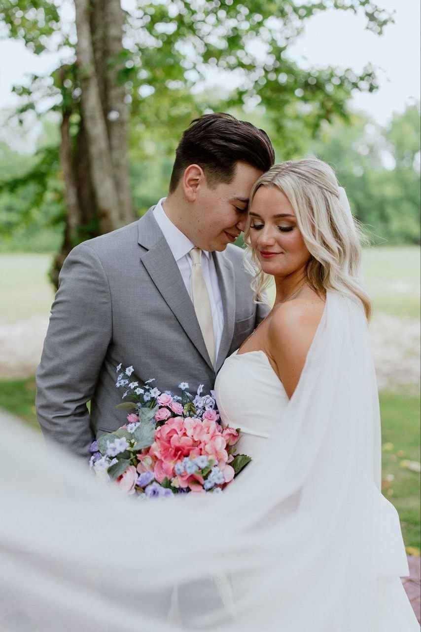 Bride and groom share a quiet moment, forehead to forehead, beneath the trees